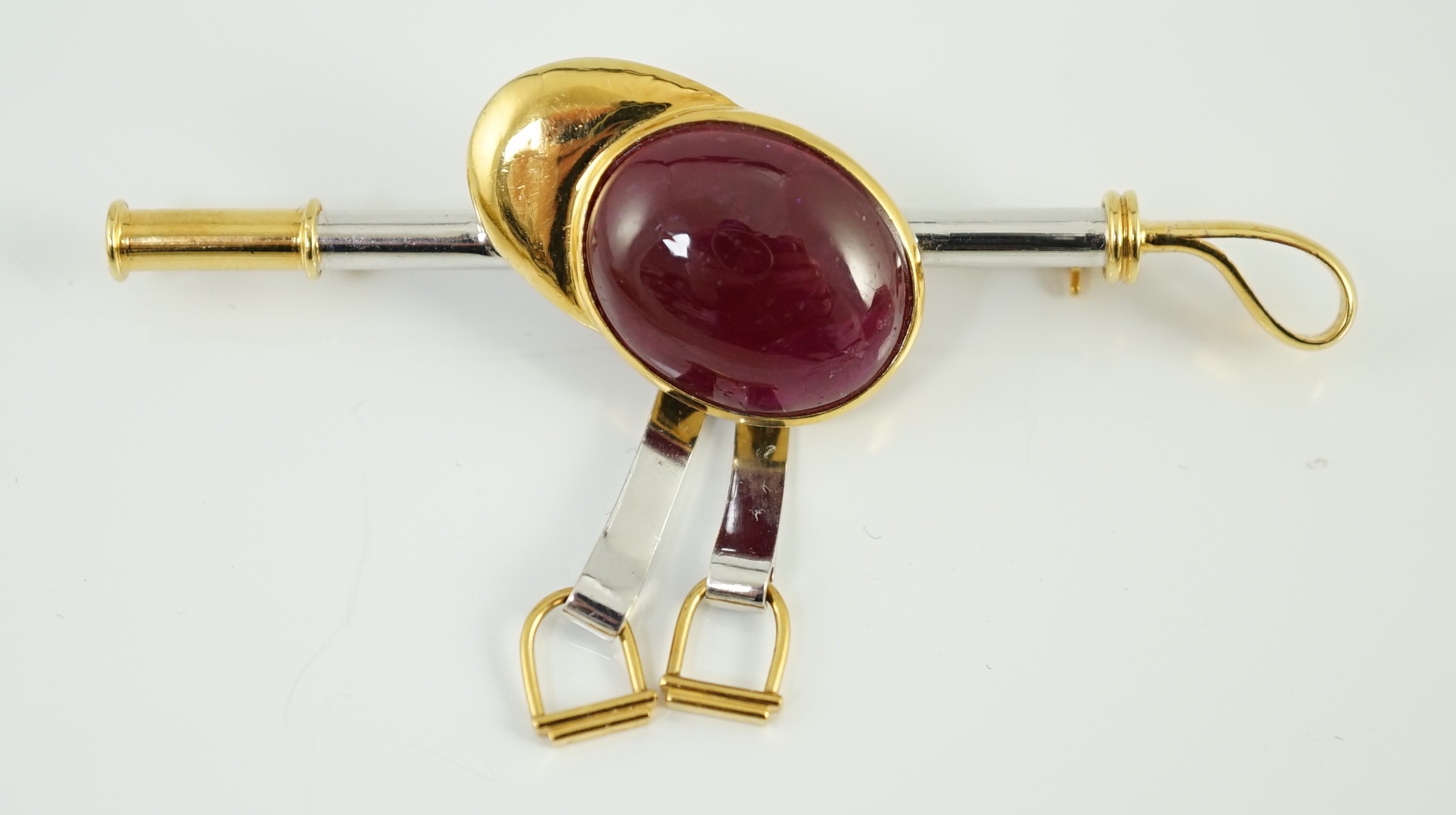 A late 20th century 18ct yellow and white gold, cabochon ruby set ‘jockey cap, riding crop and stirrups’ drop bar brooch